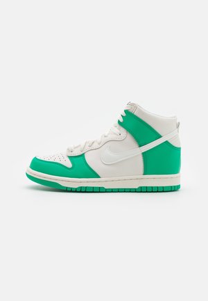 High-top sneaker i hvid og grøn med hvide snørebånd og en sål med grønt mønster, vist fra siden på en ensfarvet baggrund.
