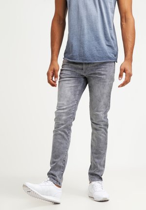Jeans en denim gris avec une finition délavée, coupe slim et design à cinq poches. Associés à un T-shirt bleu dégradé et des baskets blanches.