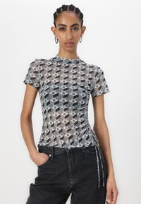 Gray and black patterned mesh top with short sleeves, round neckline, and side ruching details, paired with high-waisted dark jeans.