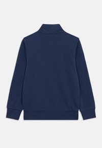 Μπλε ναυτικό μακρυμάνικο πουλόβερ με ψηλό γιακά, ριμπ μανσέτες και μέση, εμφανίζεται από πίσω σε λευκό φόντο.