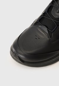 Black athletic shoe with a smooth leather upper, mesh panels, rounded toe, and subtle branding. Features textured details for grip.