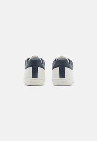 Sneakers in pelle sintetica blu con suola in gomma bianca. Presentano un pannello posteriore blu a contrasto e il nome del marchio impresso sul tallone.