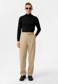 Zwarte coltrui, beige high-waisted broek met een riem en zwarte enkellaarsjes. Minimalistisch ontwerp en gladde texturen.