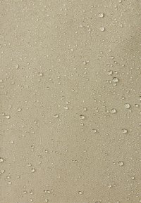 Suprafață din țesătură bej texturată cu picături de apă răspândite care se adună la suprafață, indicând rezistență la apă.