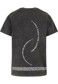 Čierne tričko s krátkym rukávom vyrobené z bavlny, s krivými bielymi textovými grafikami na chrbte a textúrovaným, umývaným povrchom.