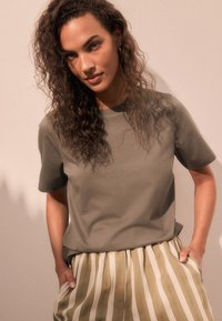 Maglietta verde oliva in tessuto morbido, abbinata a pantaloni a righe fluidi nei colori oliva e crema. Vestibilità casual con maniche corte.