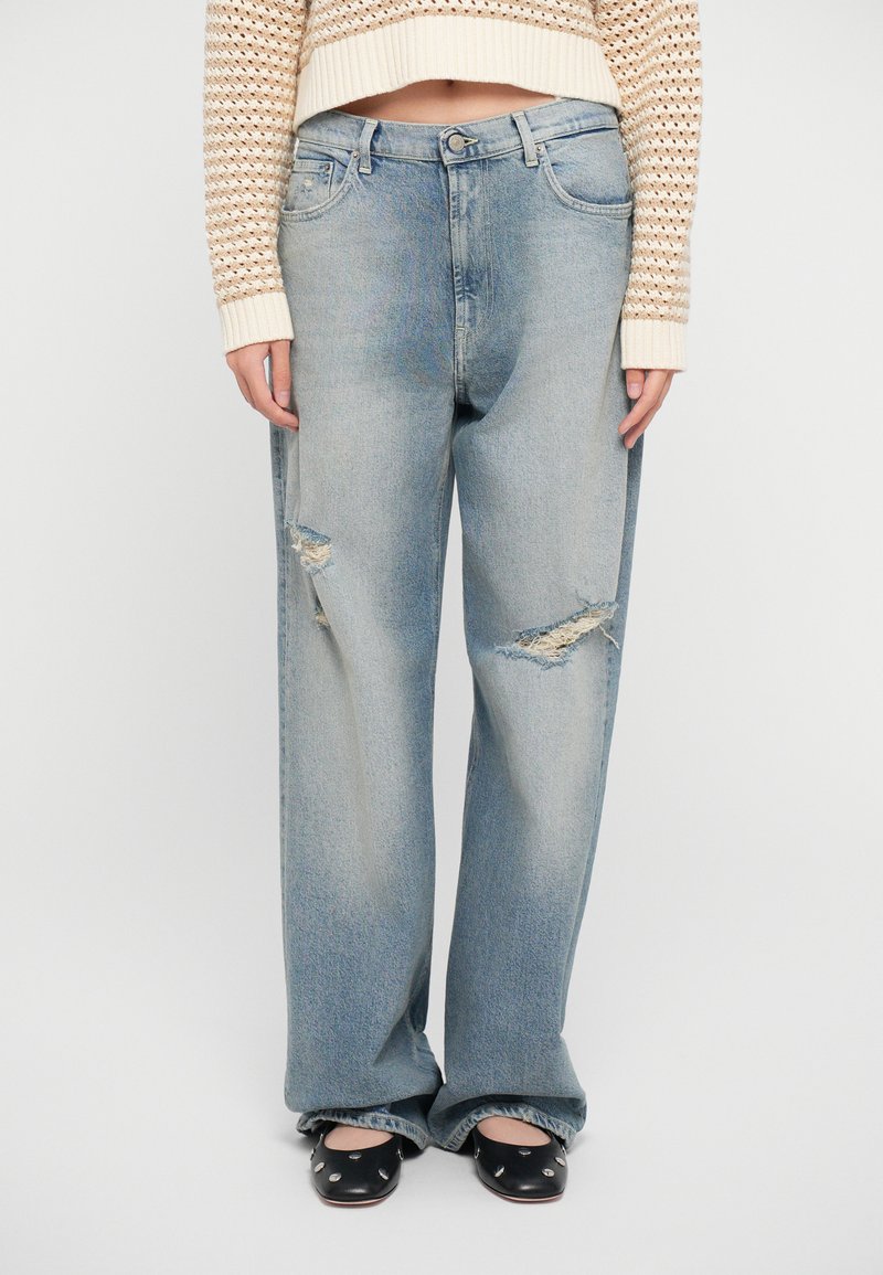 Light blue, high-waisted, wide-leg jeans with distressed patches. Soft denim material with fading, featuring five pockets and a belt loop.