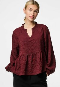 Bordeaux struktureret tunika top med en flæsekant i halsen, lange ærmer og en udvidet kant. Stoffet har et let krøllet udseende.