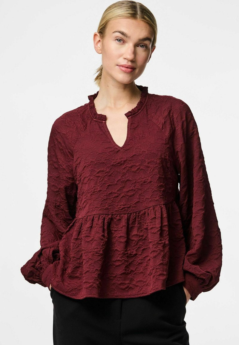 Bordeaux struktureret tunika top med en flæsekant i halsen, lange ærmer og en udvidet kant. Stoffet har et let krøllet udseende.