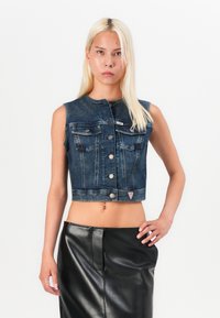 Kratka temno modra denimska jakna s ovratnikom, sprednjimi žepi in srebrnimi gumbi. V kombinaciji z črno usnjeno krilom. Gladka tekstura.