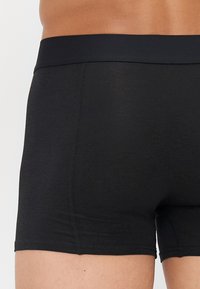 Boxers en coton noir avec une ceinture lisse, design légèrement ajusté et détails de couture subtils. Le tissu a une texture douce.