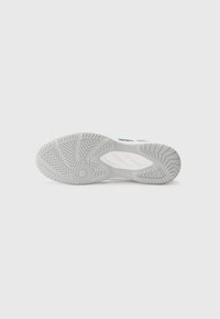 Semelle de chaussure de sport blanche avec un grip texturé, présentant un motif circulaire au talon et des nervures en zigzag pour l'adhérence.