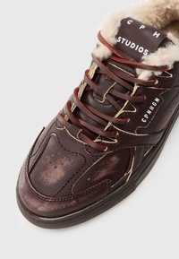 Mørkebrune lærersneakers med røde snørebånd, cremefarvet lammeskindforing, og hvid "CPH STUDIOS" og "CPNHGN" branding.