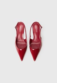 Talons slingback en cuir verni rouge et brillant avec bout pointu et talon fin. Comprend une lanière réglable et des semelles rembourrées.