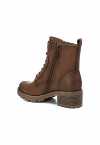 Botín de cuero marrón hasta el tobillo con cremallera, parte delantera con cordones, tacón texturizado y suela resistente. Presenta un tirador en la parte posterior para facilitar su uso.