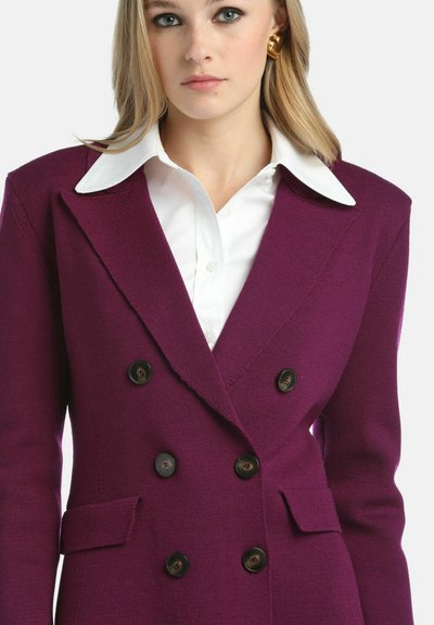 Vijoličast dvoredni blazer s vrhunskimi reverji, teksturirano blago in črnimi gumbi. Usklajen z belo srajco z ostrim ovratnikom.