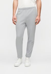 Ανοιχτό γκρι φόρμα με ελαστική μέση, σχεδιασμό στενών ποδιών και απαλό ύφασμα, σε συνδυασμό με λευκά αθλητικά παπούτσια.