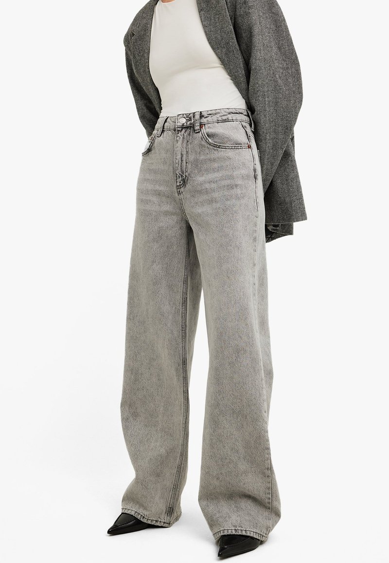 Light gray wide-leg jeans made from denim, featuring a high waist, front pockets, and visible stitching details, paired with black shoes.