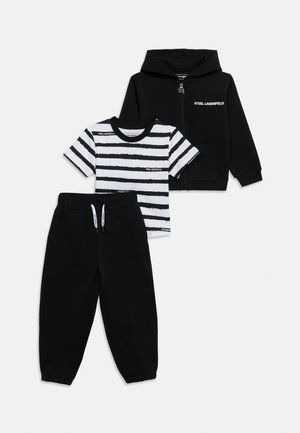 Svart hettejakke med glidelås, svarte bukser med snor, og kortermet svart-hvitt stripet T-skjorte med "Karl Lagerfeld" merke.