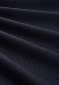 Donkerblauwe stof met een gladde textuur, gekenmerkt door opgevouwde lagen die zachte, vloeiende golven creëren. Minimaal glans en geen zichtbare patronen.