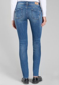 Jean skinny bleu en denim, avec deux poches arrière, un patch en cuir à la taille et une texture lisse.