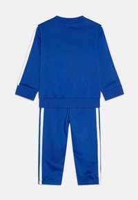 Chándal azul hecho de una tela suave; cuenta con mangas largas, rayas blancas a los lados, puños elásticos y pantalones ajustados a juego con puños en los tobillos.