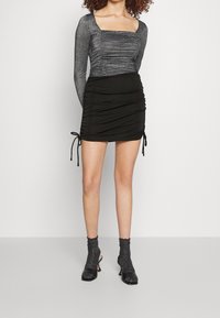 Mini falda negra fruncida con lados ajustables, combinada con una blusa plateada fruncida de manga larga, que cuenta con un escote cuadrado y una tela texturizada.