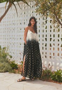 Robe maxi dégradé noir et crème, à coupe loose, avec des fentes sur les côtés et un motif géométrique en or, fabriquée dans un tissu léger.