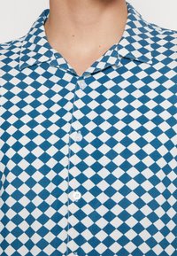 Chemise à carreaux bleue et blanche avec un col boutonné, des boutons sur le devant et une texture de tissu lisse.
