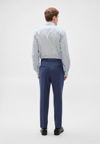 Μπλε παντελόνι φόρμας ανδρών και μπλε-λευκό ριγέ πουκάμισο με μακριά μανίκια. Το πουκάμισο έχει γιακά με κουμπιά και το παντελόνι διαθέτει πίσω τσέπες.