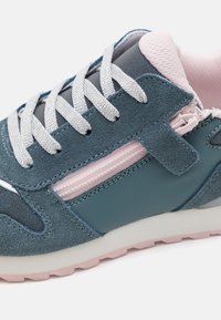 Sportsko sneaker med en blå semsket overdel, rosa detaljer, en hvit mesh-tunge og flate hvite lisser, med en teksturert gummisåle.