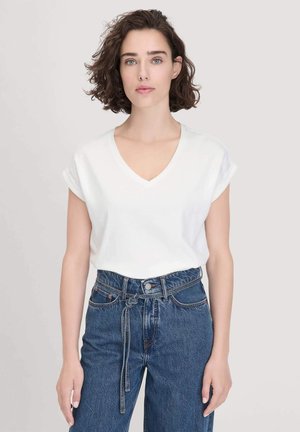 Weißes V-Ausschnitt-T-Shirt mit umgeschlagenen kurzen Ärmeln, kombiniert mit hochgeschnittenen blauen Jeans mit einer gebundenen Detail am Bund.