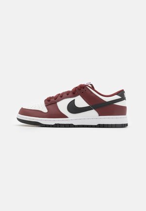 Sneaker basse bianche e rosso scuro con logo swoosh nero e suola nera, mostrata dal lato esterno su sfondo bianco.