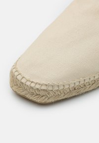 Espadrille en toile beige à bout pointu, avec une semelle en corde de jute et des détails cousus le long du bord. Texture lisse.