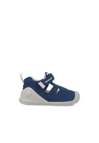 Blauer fabric Schuh mit geschlossenem Zeh, verstellbarem Riemen und weißer Gummisohle mit leichter Textur; enthält ausgeschnittene Verzierungen.
