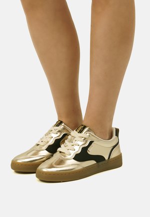 Zapatillas metálicas doradas con acentos negros, suela de goma texturizada, diseño de cordones y cuello acolchado. Elegantes y modernas con colores contrastantes.