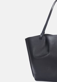 Sac cabas en cuir noir avec une finition texturée, une forme souple et une seule longue anse. Présente un léger pli décoratif en haut.