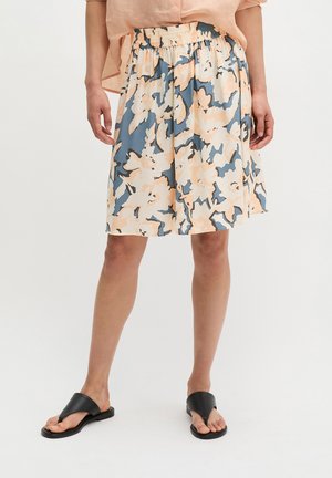 Jupe longueur genou avec taille élastique en motif floral beige et bleu, portée avec un chemisier pêche clair et des sandales noires ouvertes aux orteils.