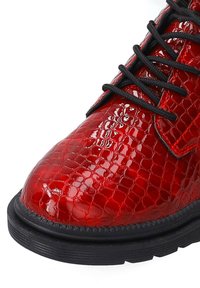 Red synthetic lace-up boot featuring a shiny snakeskin texture, black laces, and a textured black rubber sole.