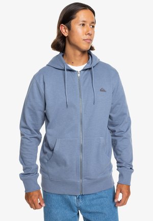 Niebieska bluza z kapturem zapinana na zamek, wykonana z miękkiego materiału, z przednią kieszenią, regulowanymi sznurkami i małym logo na lewej piersi.