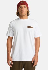 Hvid bomulds-T-shirt med korte ærmer og rund halsudskæring. Har et brunt og orange logo-patch på venstre bryst.