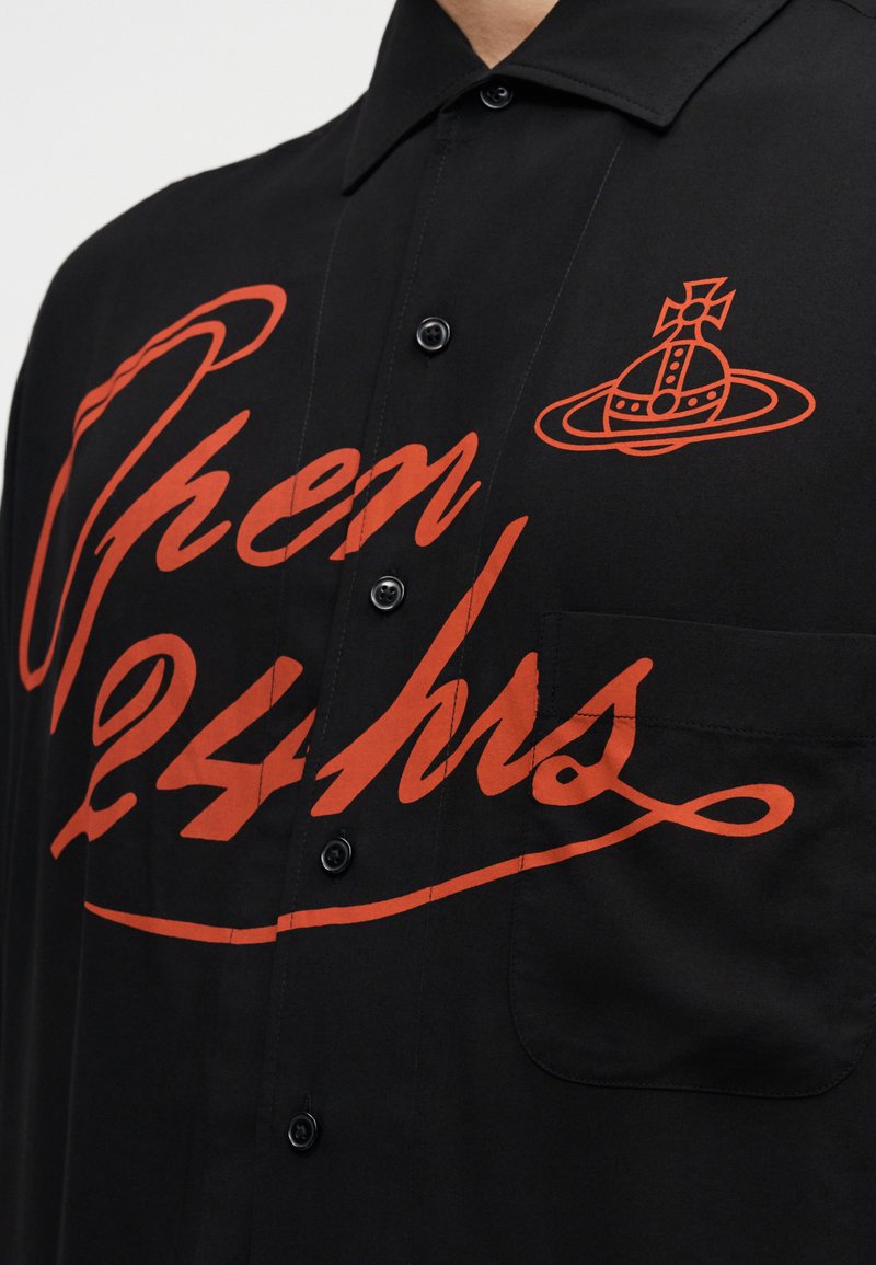 Chemise noire boutonnée avec une grande impression rouge indiquant "Ouvert 24h/24" et un logo graphique. Comprend une poche poitrine et un tissu à la texture douce.