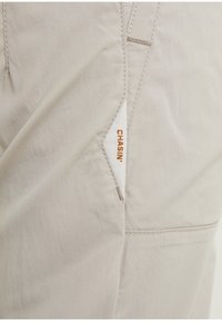 Tissu beige avec une petite étiquette blanche affichant le mot "CHASIN" en couture orange près d'une couture.