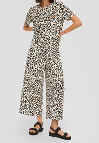 Bluzka w panterkę i szerokie spodnie w kolorze kremowym, z pomarańczowymi i czarnymi akcentami. Całość uzupełniają czarne platformy.