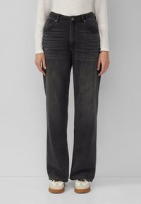 Jeans in denim neri a gamba larga con una leggera trama sbiadita, dotati di cinque tasche, zip e passanti per cintura. Abbinati a sneakers bianche.