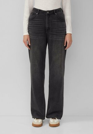 Wijduitlopende zwarte denim jeans met een lichte vervaagde textuur, voorzien van vijf zakken, een ritsenluiting en riemlussen. Gepaard met witte sneakers.