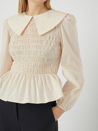 Helles beige Peplum-Top mit gefüttertem Oberteil, großem flachem Kragen und gerafften langen Ärmeln, aus einem weichen, strukturierten Stoff.