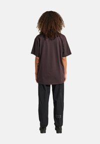 Ciemnobrązowy, oversize, krótko rękawowy T-shirt, zestawiony z czarnymi, teksturowanymi spodniami, które mają nadrukowany detal "223".