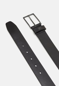 Cintura in pelle nera con una trama liscia, fibbia metallica rettangolare e numerosi fori per la regolazione. Logo embossato discreto sulla fibbia.