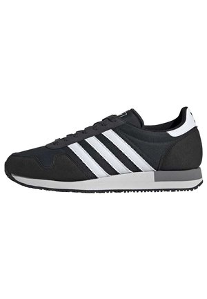 Baskets Adidas basses noires et blanches avec trois bandes blanches, lacets noirs et semelle grise et blanche.